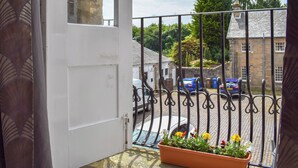 Un balcon avec une porte blanche, une rambarde en métal et un pot de fleurs.