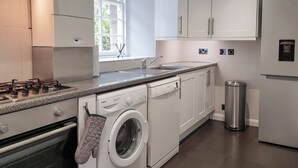 Une cuisine moderne avec des meubles blancs, un four encastré, un lave-linge et un évier en acier inoxydable.