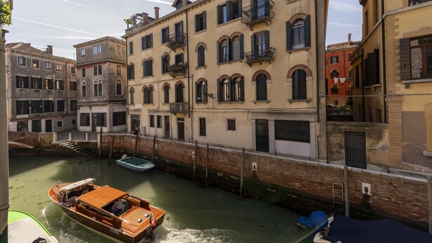 A canal with boats, historic buildings, and a wooden boat with a canopy. - Ca di Malta Room 5 by Wonderful Italy (Venice)