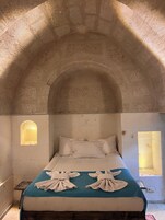 A room with a bed, two windows, and a stone ceiling.