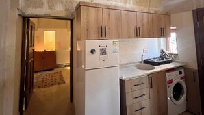 A compact kitchen with a refrigerator, a washing machine, and wooden cabinets. - Uluyol Stone House (Avanos)
