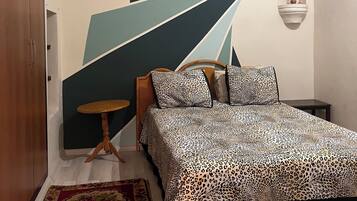 Een slaapkamer met een bed, een klein tafeltje, een decoratief vloerkleed en een kunstwerk aan de muur.