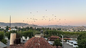 A cityscape with a clear sky, numerous hot air balloons, and a river in the foreground. - Uluyol Stone House (Avanos)