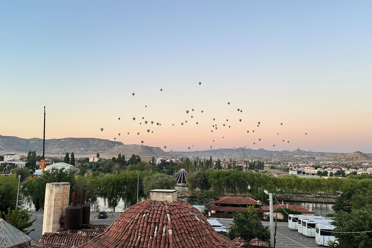 Une vue d’une ville avec un ciel dégagé, de nombreux ballons à air chaud et une rivière au premier plan.