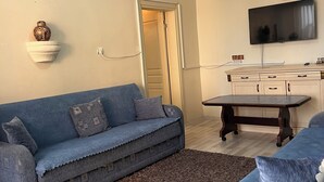 A living room with a blue sofa, a coffee table, a TV, and a patterned rug. - Uluyol Stone House (Avanos)