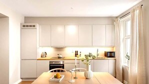 Une cuisine moderne avec des meubles blancs, un plan de travail en bois et une table à manger agrémentée d’un vase et de fruits.