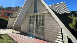 A small, single-story building with a pitched roof, a front door with glass panels, and a small porch area. - Chalé Rústico 8 min do centro turístico (Campos do Jordão)
