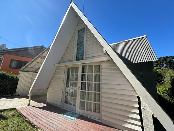 A small, single-story building with a pitched roof, a front door with glass panels, and a small porch area. - Chalé Rústico 8 min do centro turístico (Campos do Jordão)