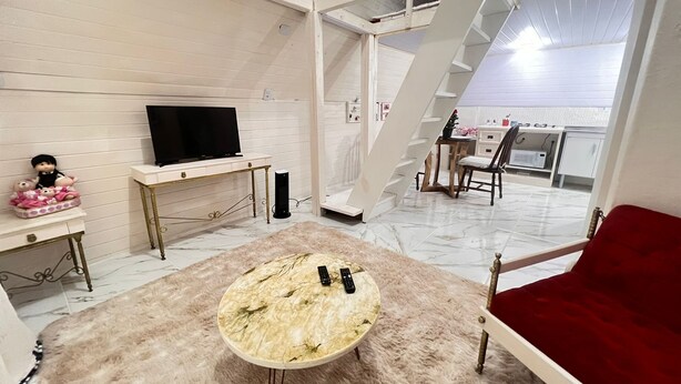 A modern living room with a TV, a small table, a red sofa, and a staircase leading to an upper level. - Chalé Rústico 8 min do centro turístico (Campos do Jordão)