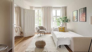 Une chambre à coucher avec un lit, une chaise, une plante et une fenêtre avec des rideaux.