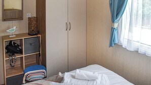 Een slaapkamer met een bed, een kledingkast, een bureau met lamp en een raam met gordijnen.