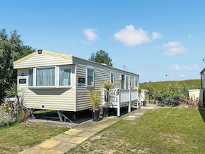 Une maison mobile dotée d’un porche couvert, d’une petite dépendance attenante et d’une cour gazonnée.