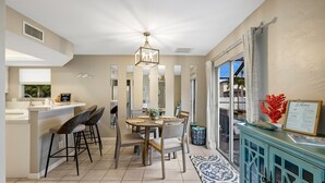Una cocina moderna con zona de comedor, que incluye una isla central con taburetes de bar, una lámpara de araña y vistas al exterior.