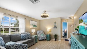 Un salón con un sofá gris, mesitas de noche verde azulado y un televisor sobre un mueble verde azulado.
