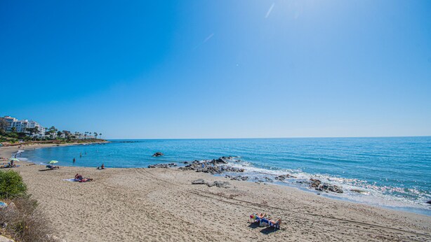 A beach with clear skies, calm water, and a few people relaxing. - Cubo's Tennis Paradise Duplex / air conditioning / free wifi / community tennis court (Mijas Costa)