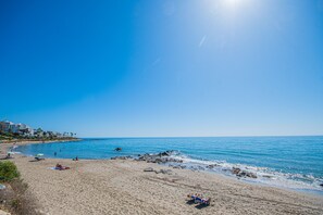 Une plage avec un ciel dégagé, une eau calme et quelques personnes qui se détendent.