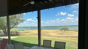Portico coperto con tavolo e sedie, affacciato su una zona erbosa con un lago e barche.