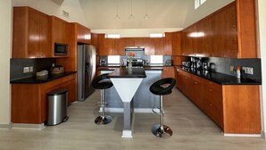 Una cucina moderna con mobili in legno, elettrodomestici in acciaio inossidabile, un'isola centrale con sgabelli da bar e illuminazione a sospensione.