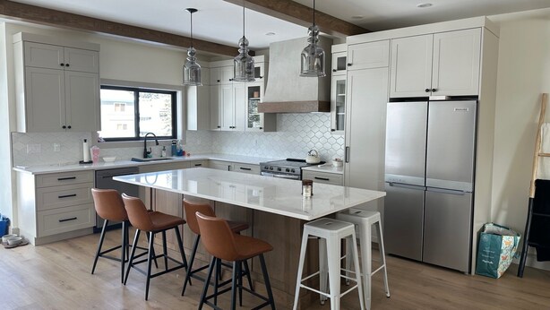 A modern kitchen with a large island, bar stools, stainless steel appliances, and a window providing natural light.