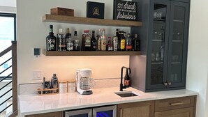 A modern kitchen with a built-in wine fridge, a coffee station, and a bar area with a sign that reads "Hand me a drink and watch me get fabulous."