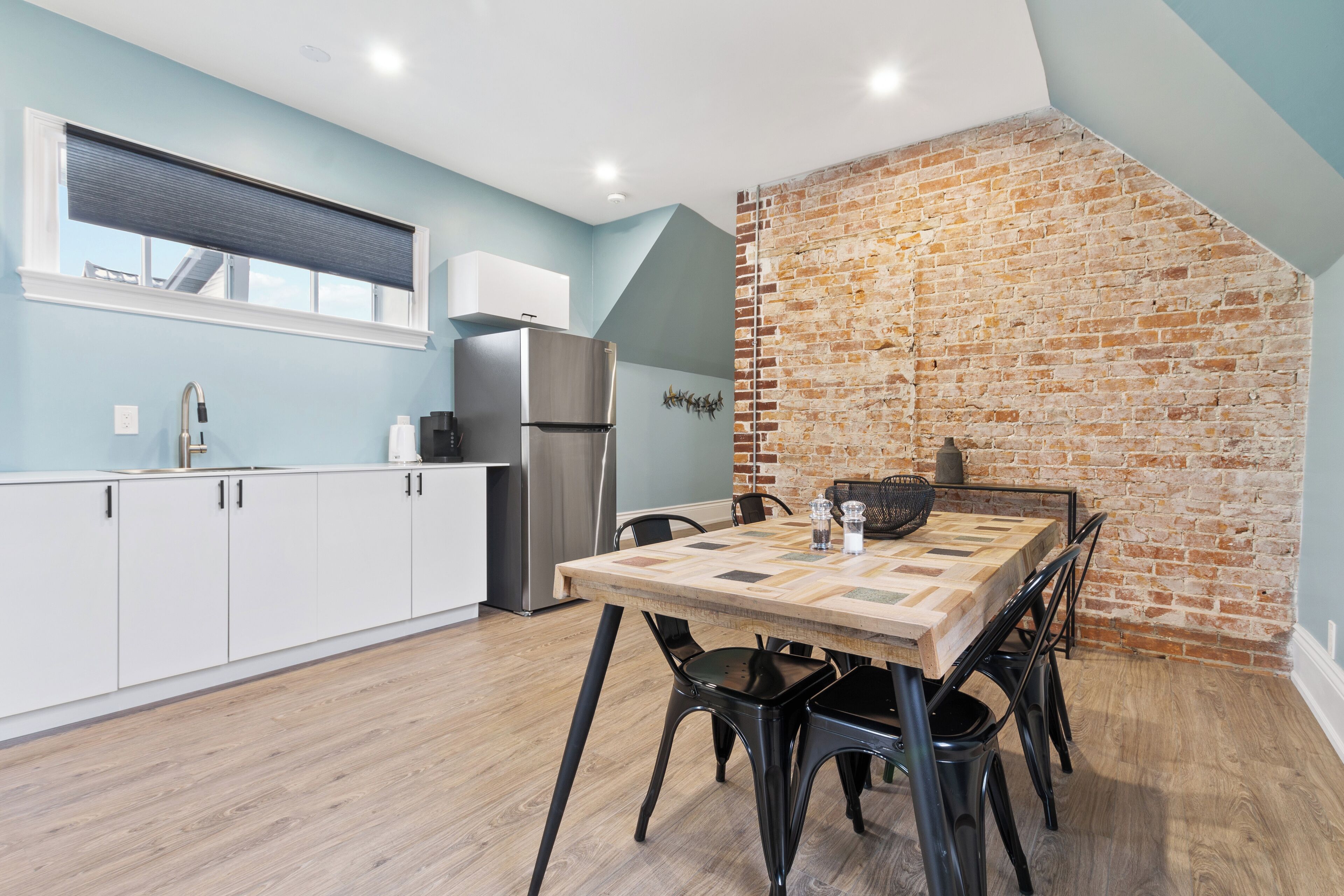 A modern kitchen with a brick wall, a wooden dining table, and black chairs.