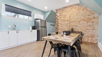 A modern kitchen with a brick wall, a wooden dining table, and black chairs.