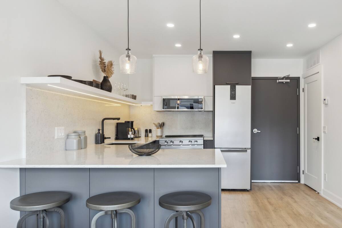 Una cocina moderna con una isla central, taburetes de bar, iluminación colgante y electrodomésticos integrados.