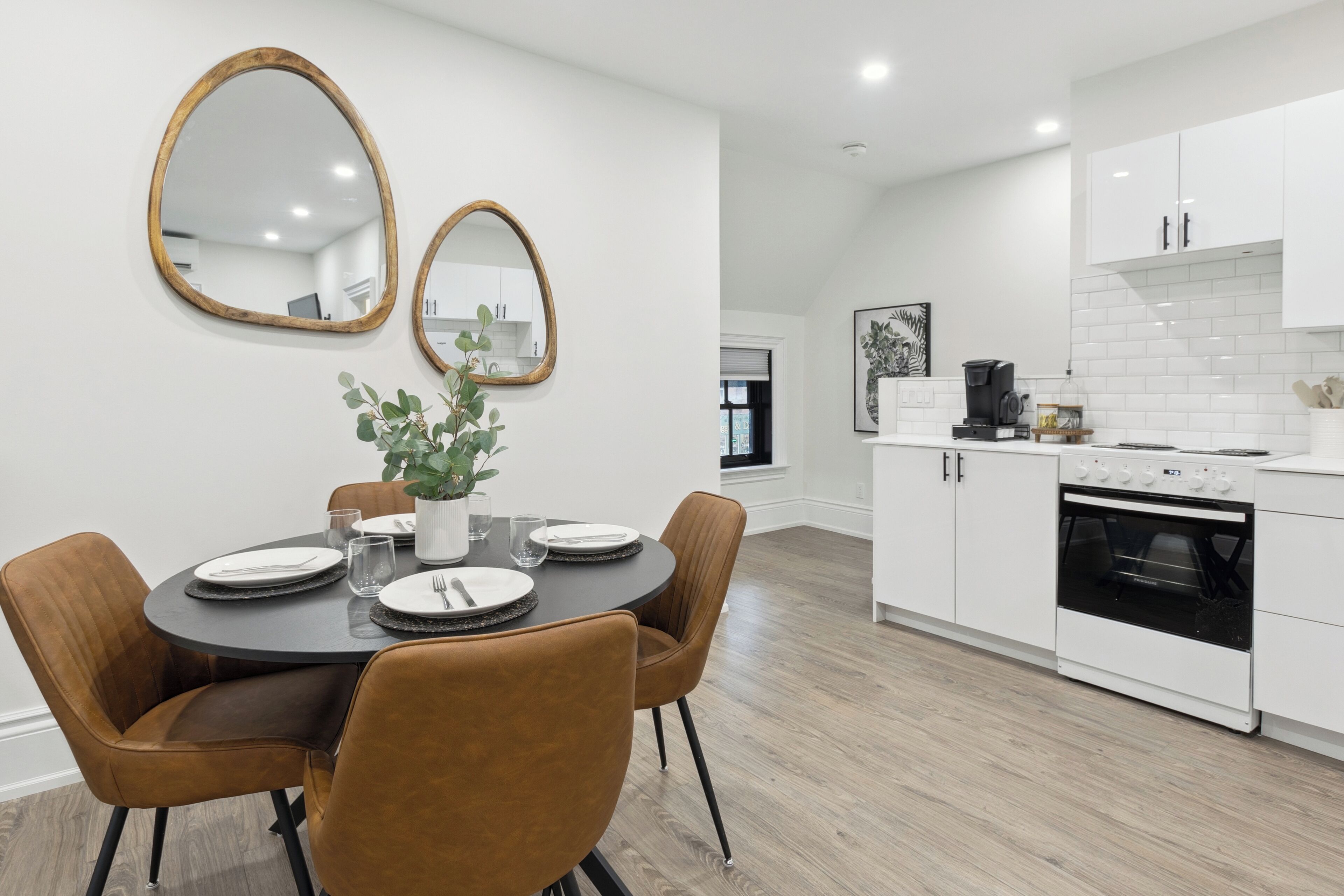 A modern kitchen with white cabinets, a black oven, and a dining area with a round table and brown chairs.