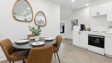 A modern kitchen with white cabinets, a black oven, and a dining area with a round table and brown chairs.