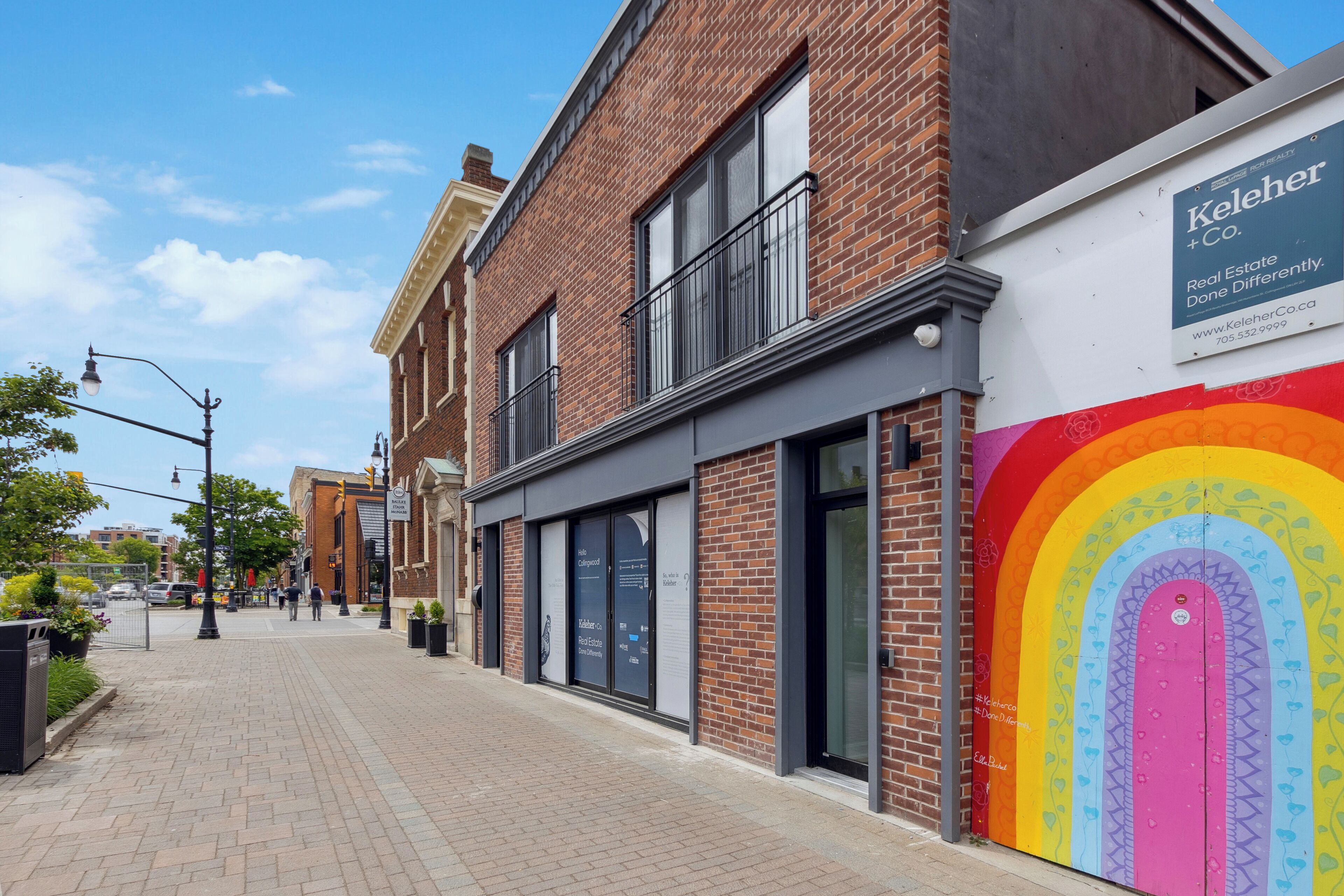 A brick building with a large glass storefront and a colorful mural on the side.