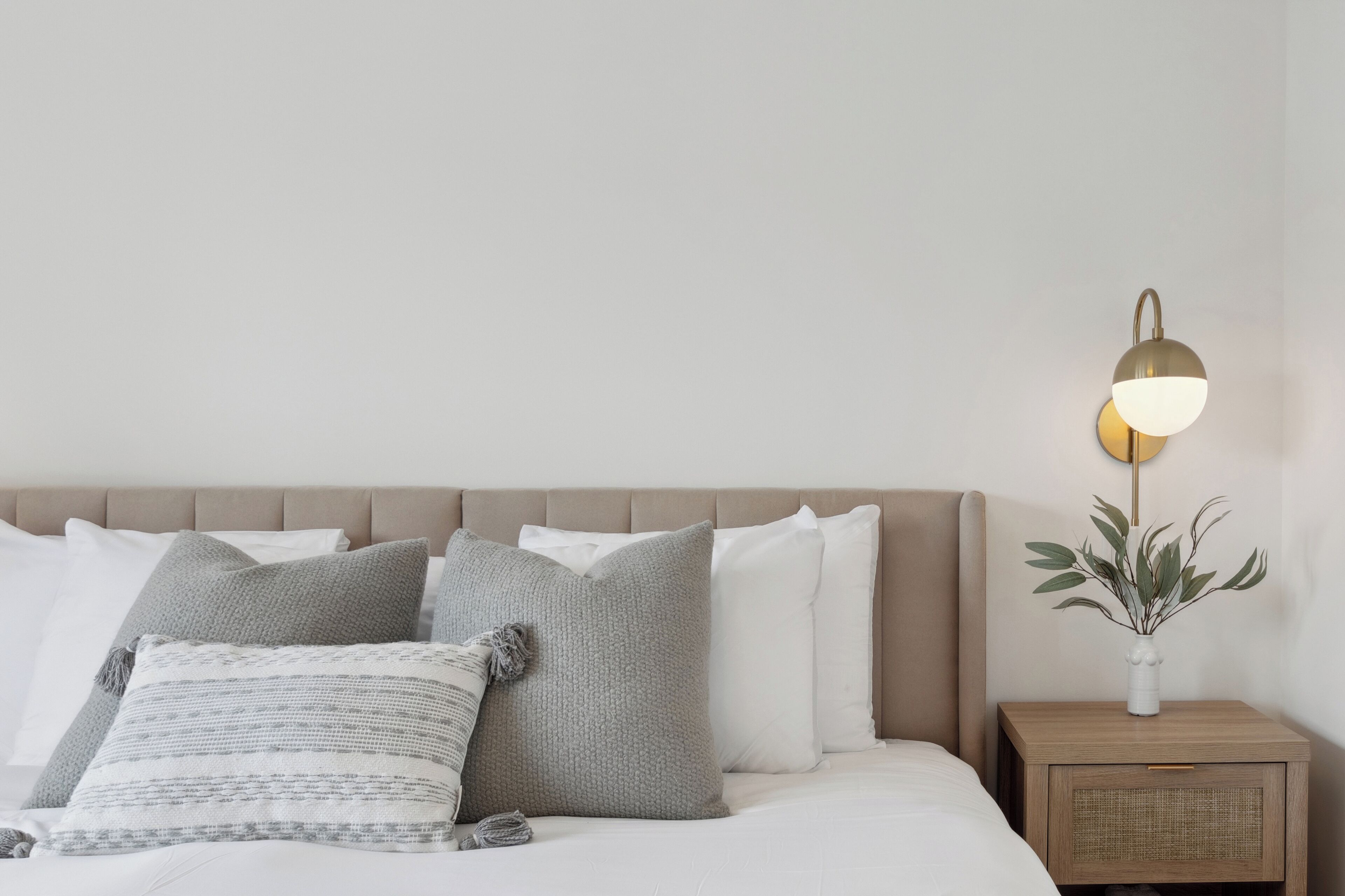 Una cama bien hecha con varios almohadones y una mesita de noche con una lámpara y un florero.