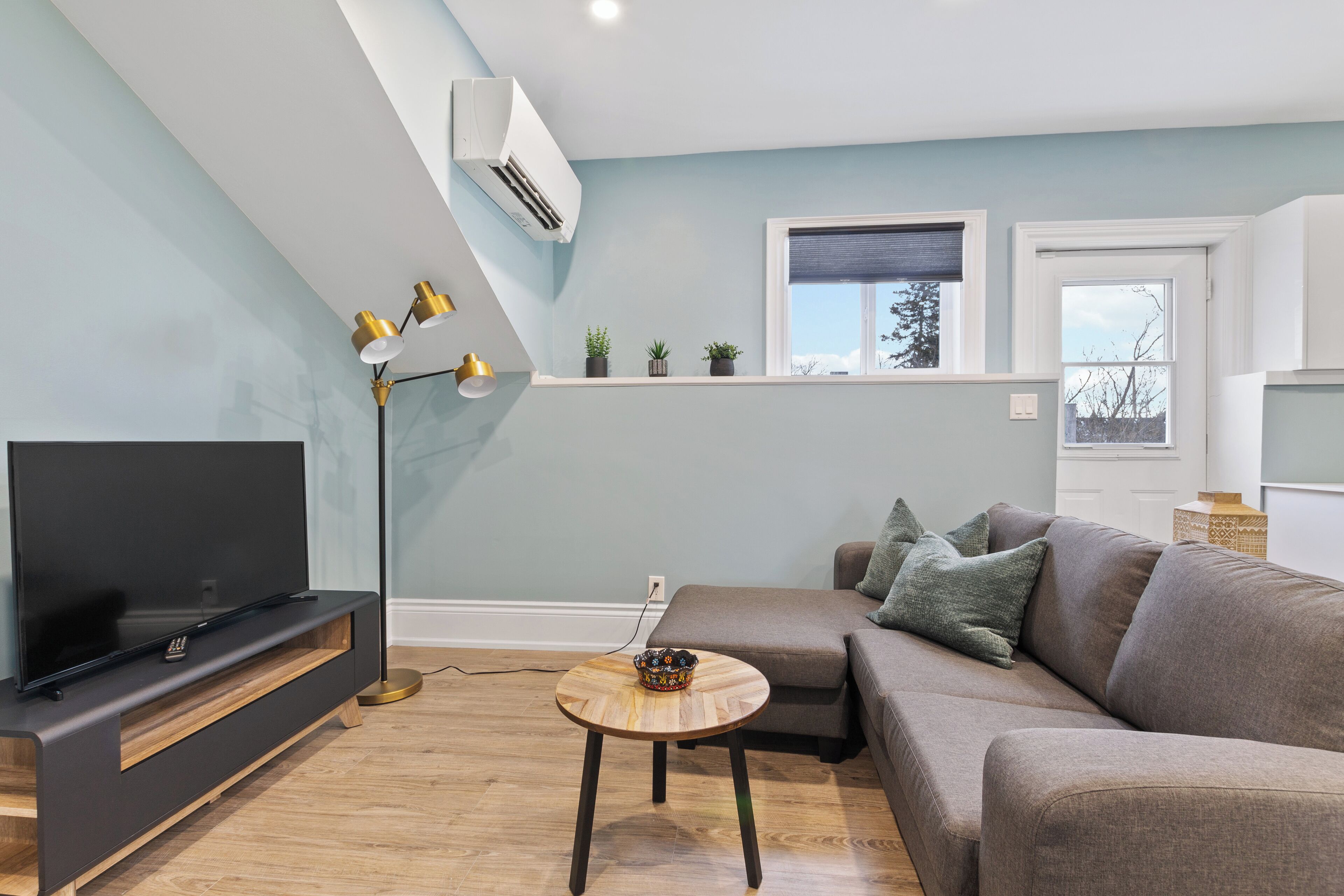 Ein modernes Wohnzimmer mit Flachbildfernseher, einer Couch, einem Couchtisch und einer Stehlampe.