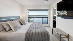 Ein Schlafzimmer mit einem großen Bett, einem Deckenventilator, Blick auf das Wasser und einer Bank am Fenster.