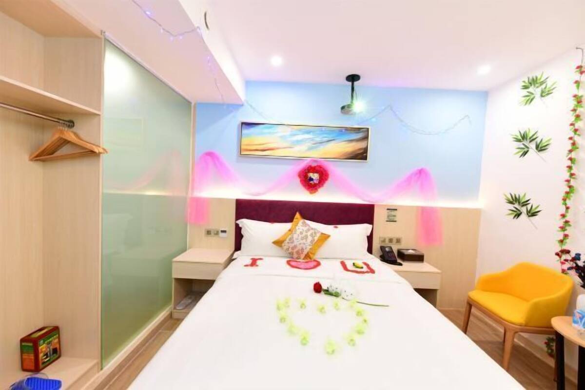 A hotel room with a bed, bedside tables, a chair, a desk, and a wall with a painting.