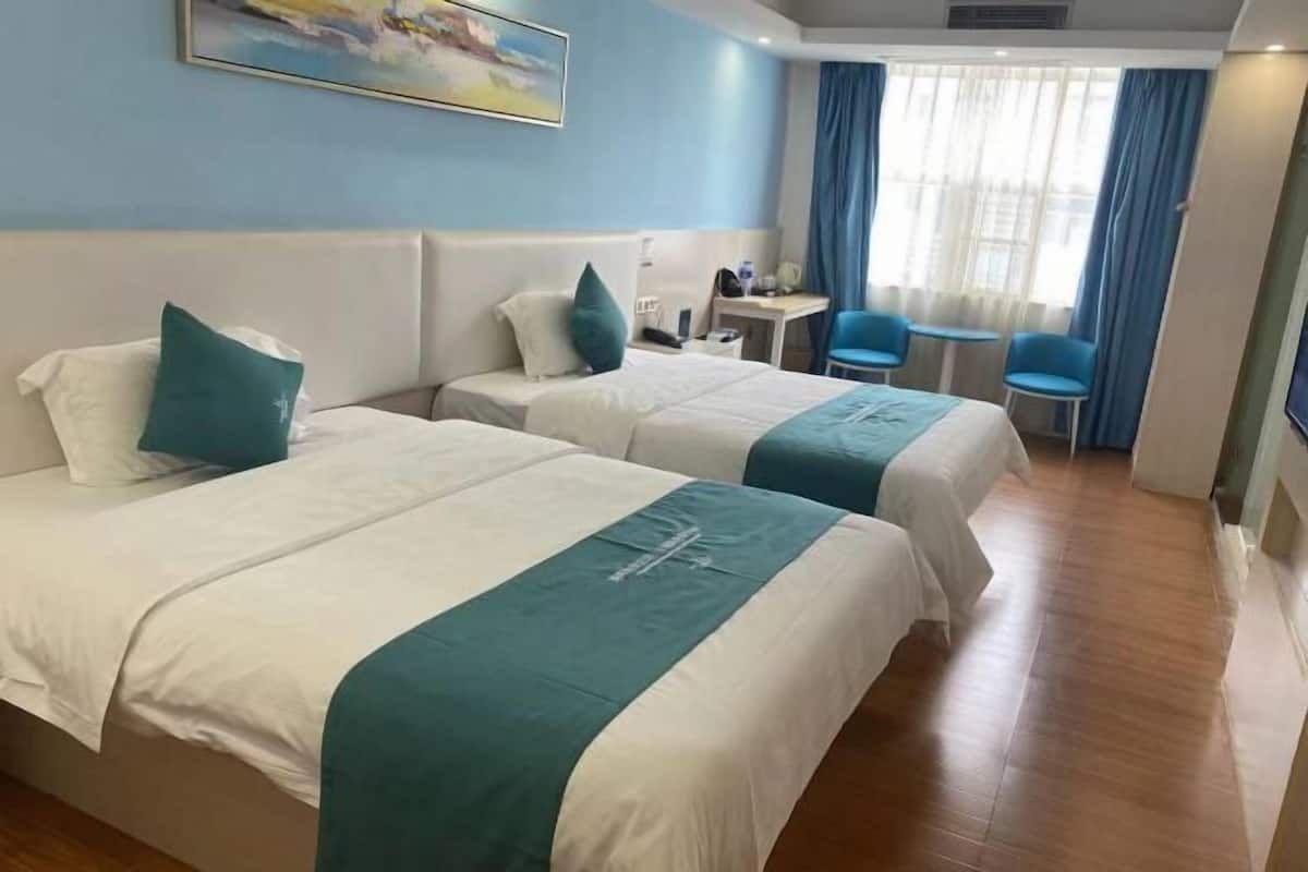 A hotel room with two beds, a desk, chairs, and a large window with curtains.
