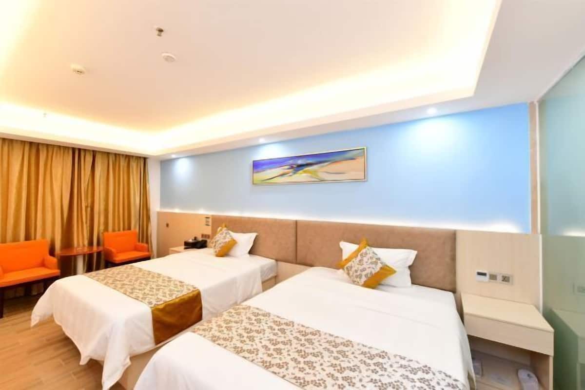 A hotel room with two beds, a desk, a chair, and a painting on the wall.