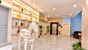 Un hall de hotel con una recepción, una escultura de un caballo blanco, estanterías con diversos objetos y una pared azul.