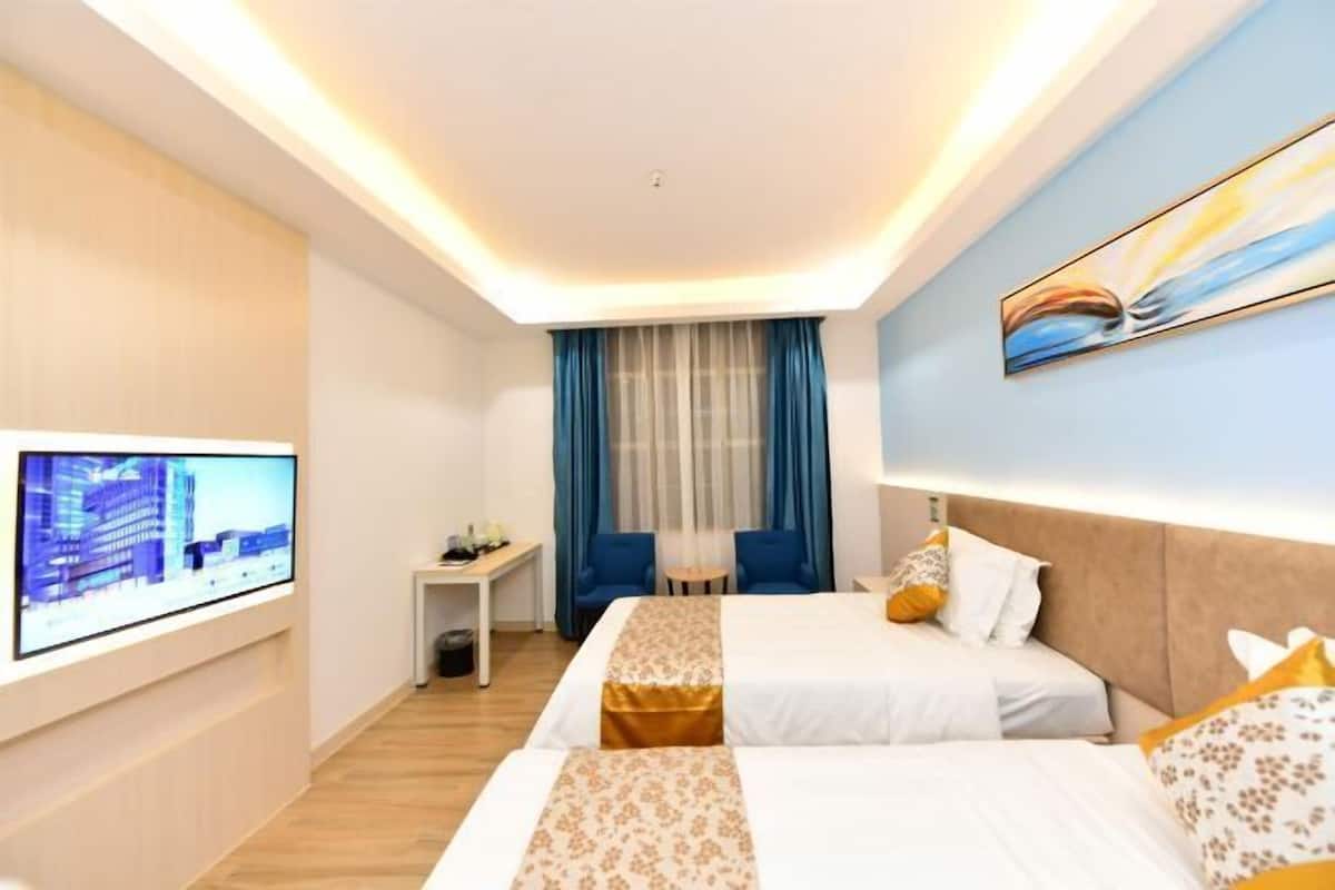 A hotel room with two beds, a TV, a desk, and a window with curtains.