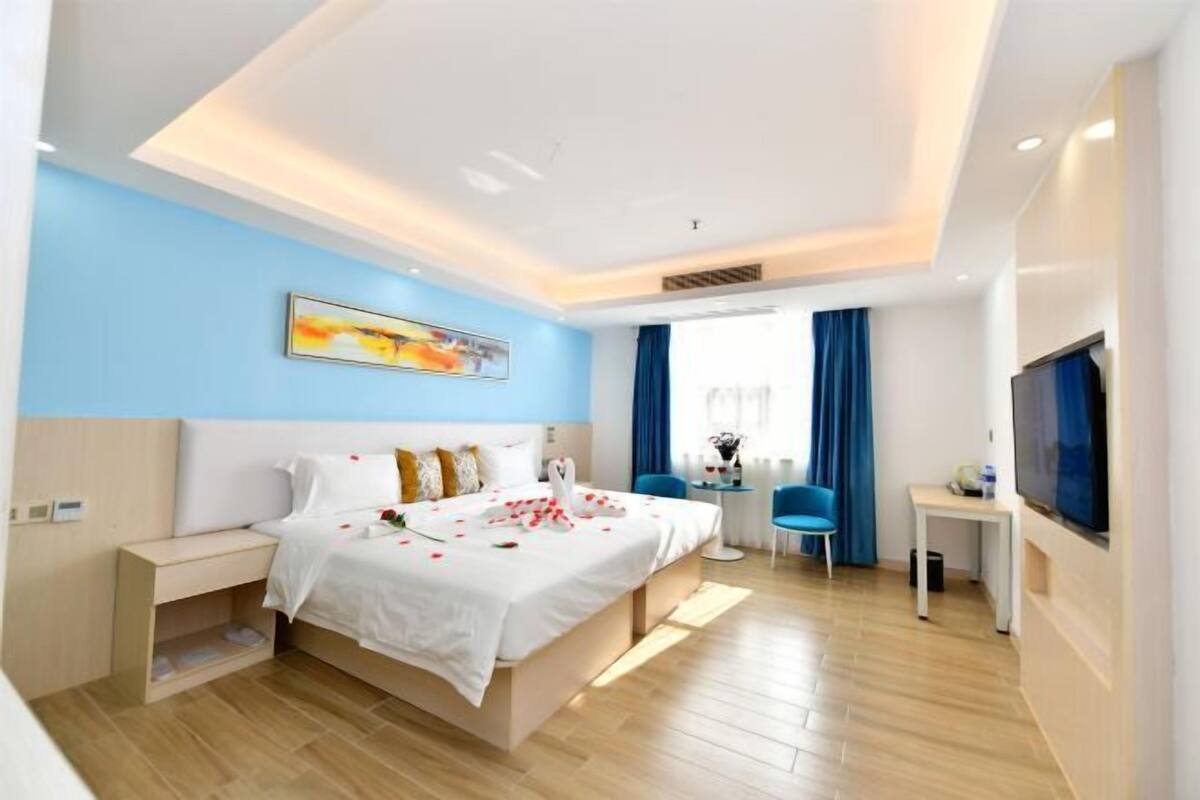A modern hotel room with a bed, bedside table, desk, chair, TV, and artwork on the wall.
