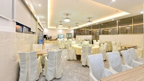Un salón de banquetes con mesas redondas, sillas blancas y un diseño moderno en el techo.