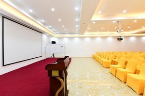 A conference room with a red carpet, rows of yellow chairs, a podium, a white screen, and ceiling lights. - Shanshui Trends Hotel (Sha Village MTR station store Guangzhou) (Guangzhou)