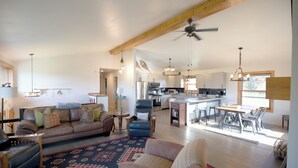 A spacious living area with a large sofa, a coffee table, and a dining table with chairs. There is a kitchen in the background with modern appliances and a ceiling fan. -  4-bedroom get away with large kitchen, patio and backyard  (Carbondale)