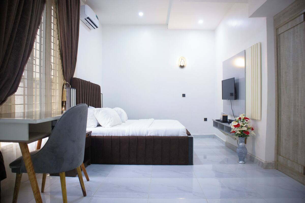 A modern bedroom with a bed, a desk, and a TV.