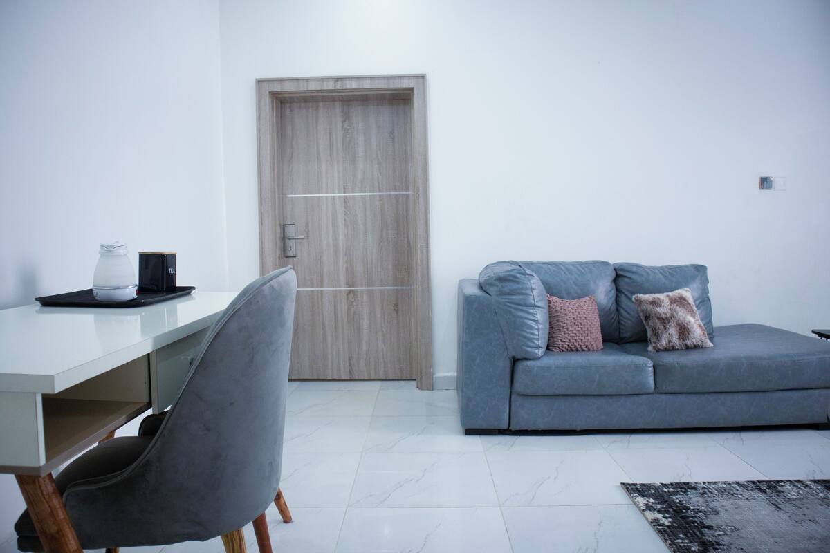 A modern living room with a grey sofa, a white desk, and a grey chair.