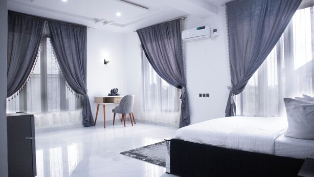 A modern hotel room with a large bed, a desk, and a chair. - Kyeston Apartment (Abuja)