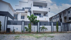 A modern multi-story residential building with a gated entrance, a small garden area, and a clear sky. - Kyeston Apartment (Abuja)
