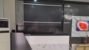 A modern reception area with a black and white desk, a marble-patterned wall, and a TV mounted on the wall. - Kyeston Apartment (Abuja)