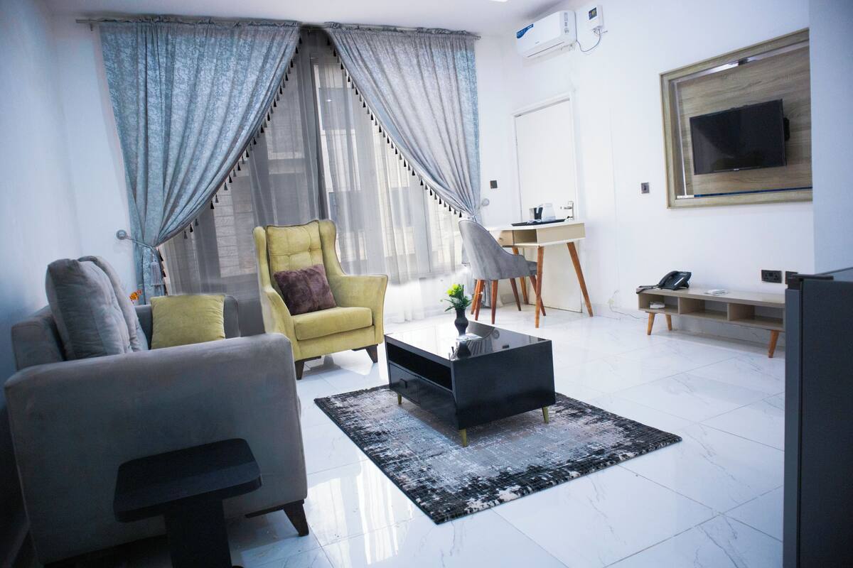 A modern living room with a sofa, armchair, coffee table, and a TV mounted on the wall.