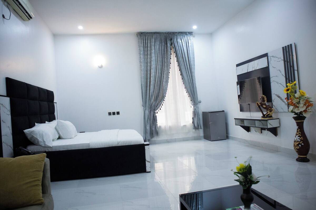 A modern hotel room with a bed, a sofa, a small table, and a decorative vase.