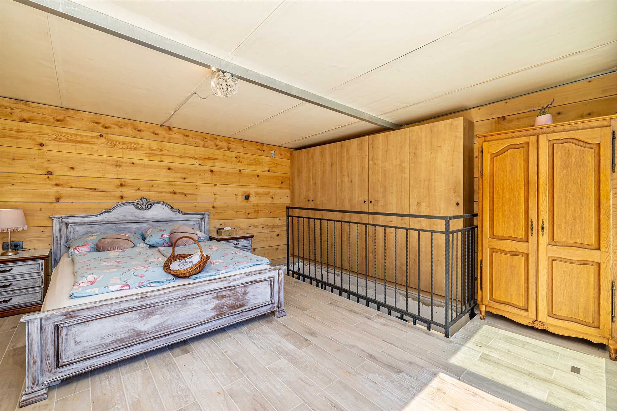 Ein Schlafzimmer mit einem Bett mit Holz-Kopfteil, einem Nachttisch, einer Kommode und einem Kleiderschrank.